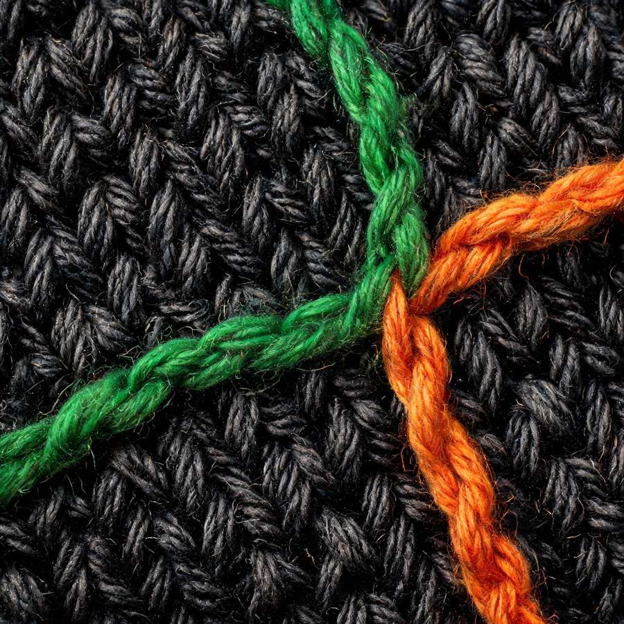Macro shot of NOSOX knitted fabric: graphite yarn with green and orange thread